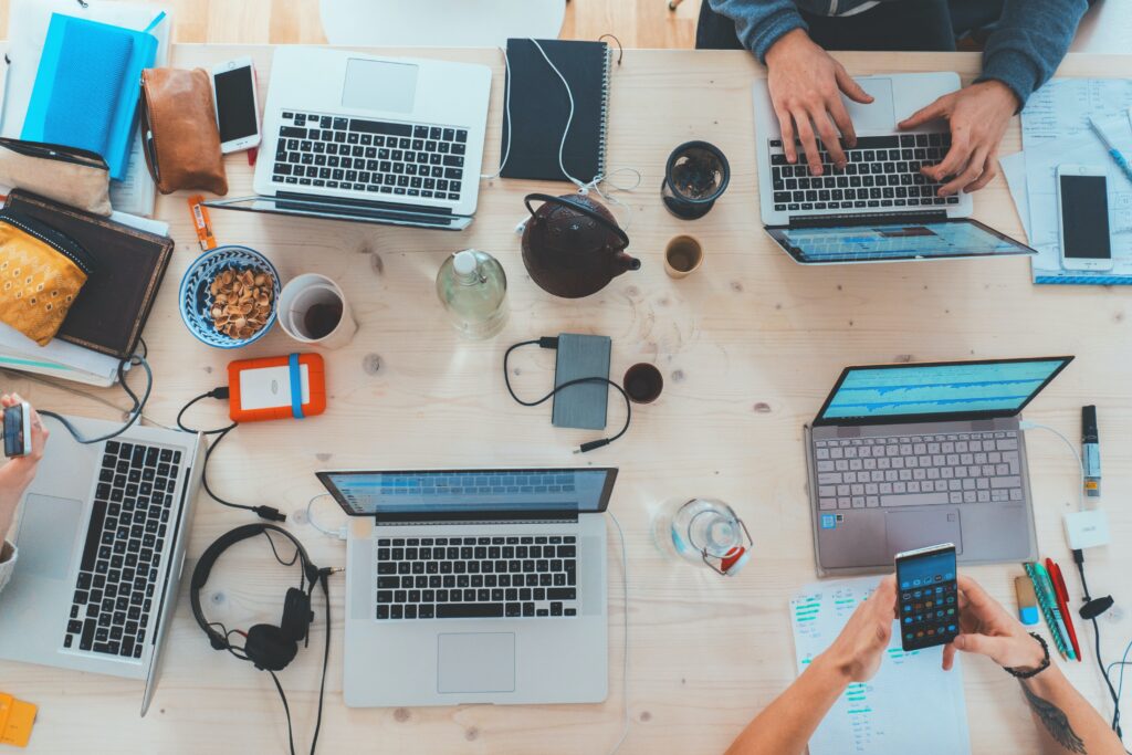 An overhead image of a table with laptops on it and other work paraphernalia with a diverse group of people sitting around the table. 