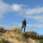 A photo of me standing on dunes in a beach in West Wales with a blue sky.