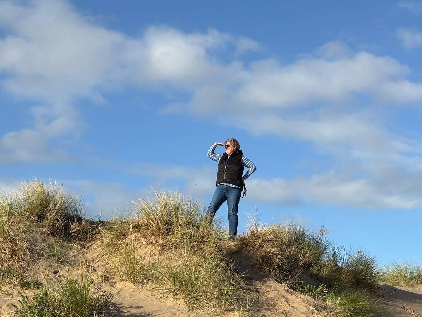 A photo of me standing on dunes in a beach in West Wales with a blue sky.