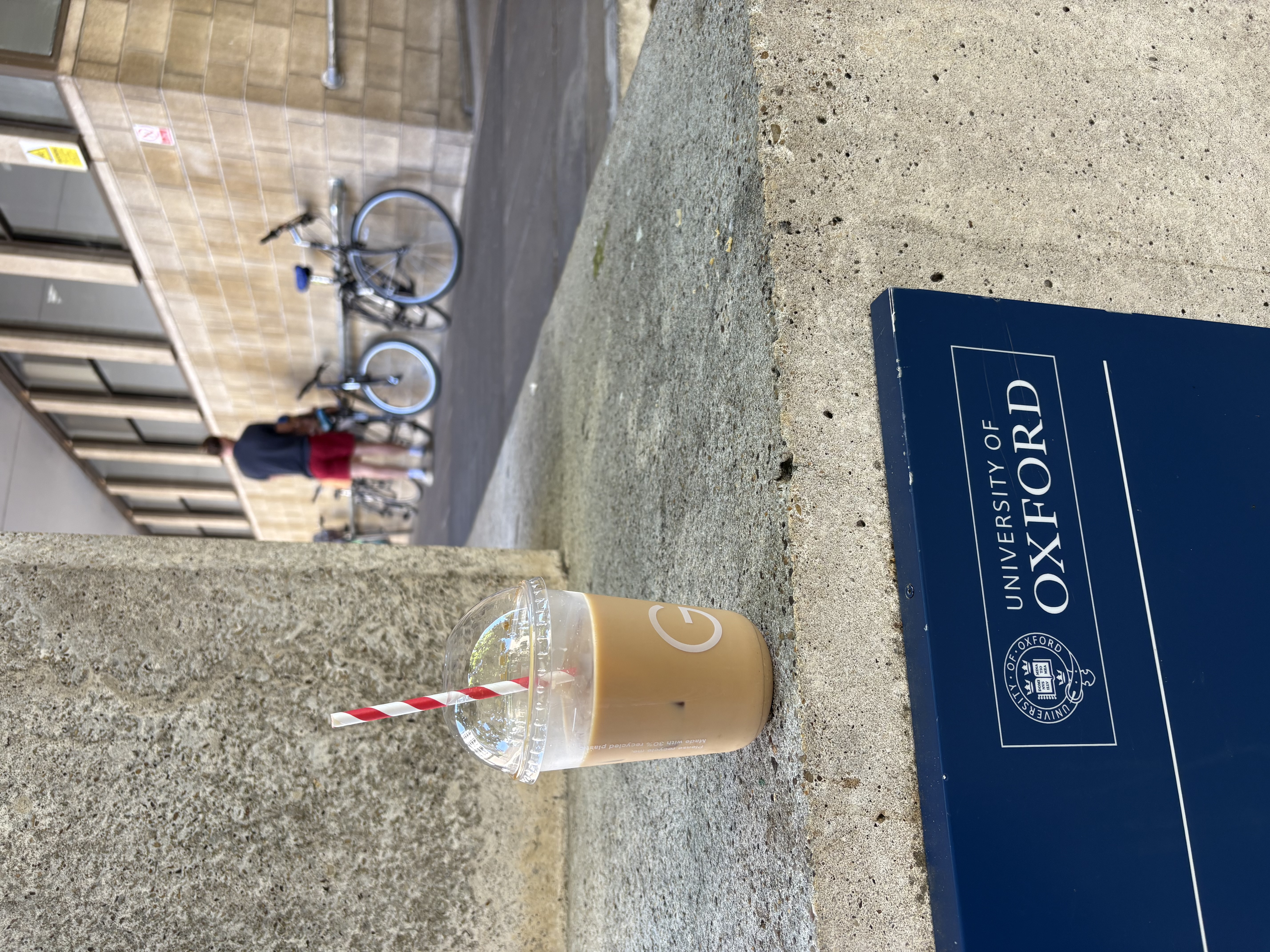 A photo of a cup of coffee, with a unviersity sign and bikes in the background